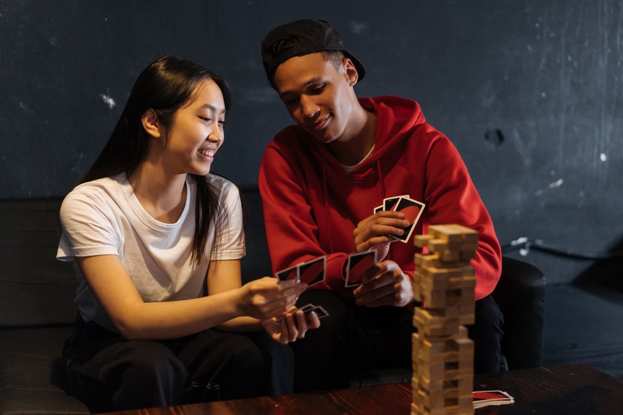 Two friends playing cards and Jenga indoors, sharing laughter and bonding over games.